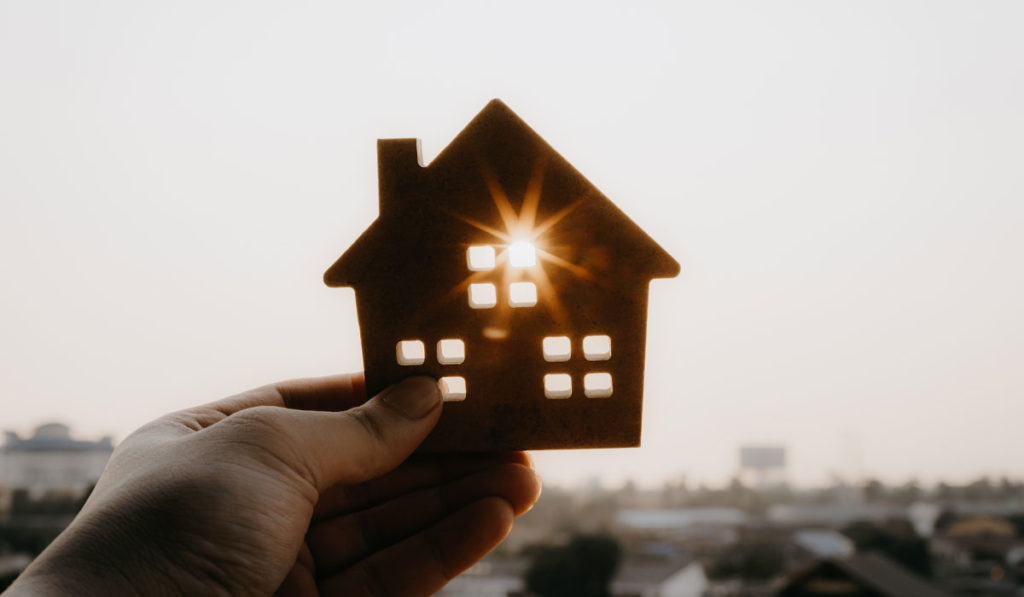 Person holding a cutout of a miniature house with sunlight coming through
